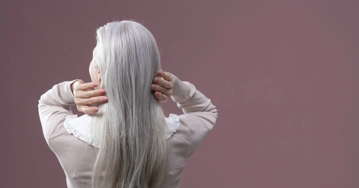 Mulher de costas passando as mãos no cabelo grisalho longo — cuidado com o cabelo na menopausa