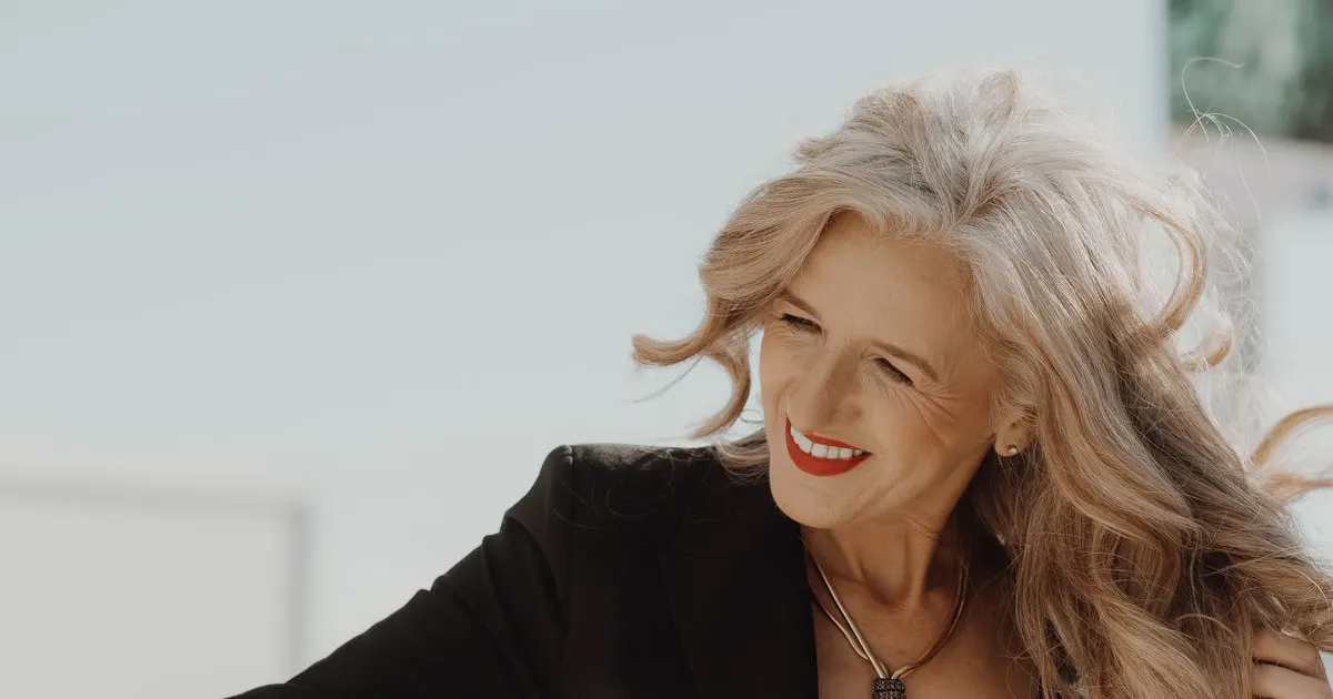 Mulher madura de cabelo grisalho sorrindo enquanto segura os fios — queda de cabelo na menopausa