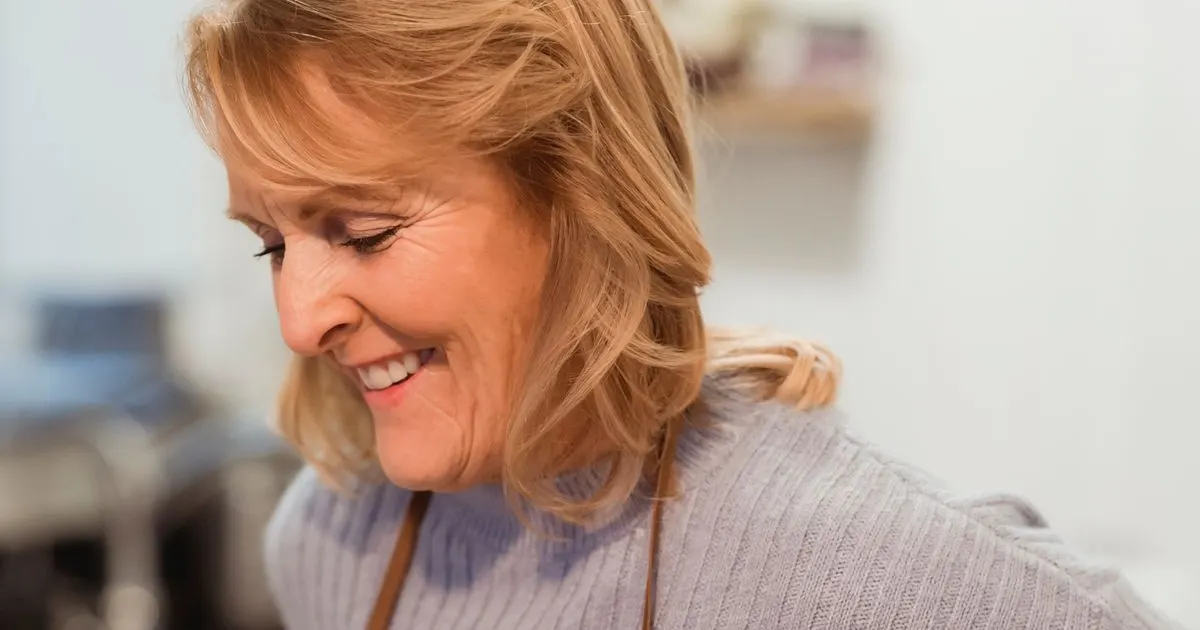 Mulher madura sorrindo na cozinha em rotina de alimentação saudável — imagem ilustrativa do artigo sobre vitaminas para cabelo